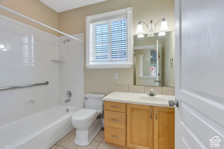 Full bathroom with a white tub-shower combination, wood-finish vanity with a light countertop, and a tiled floor