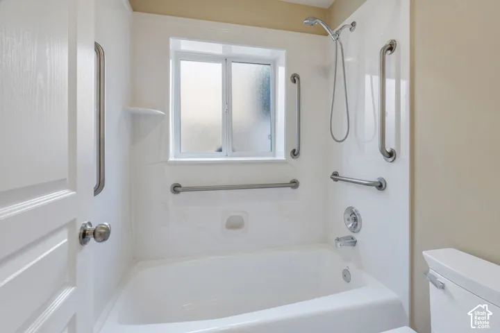 White bathtub and shower combination with chrome fixtures, integrated shelving, and frosted window