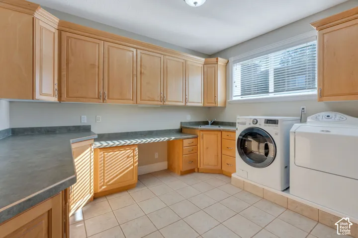 Spacious utility room featuring extensive light wood-finish cabinetry, ample countertop space, a built-in sink, and a tiled floor