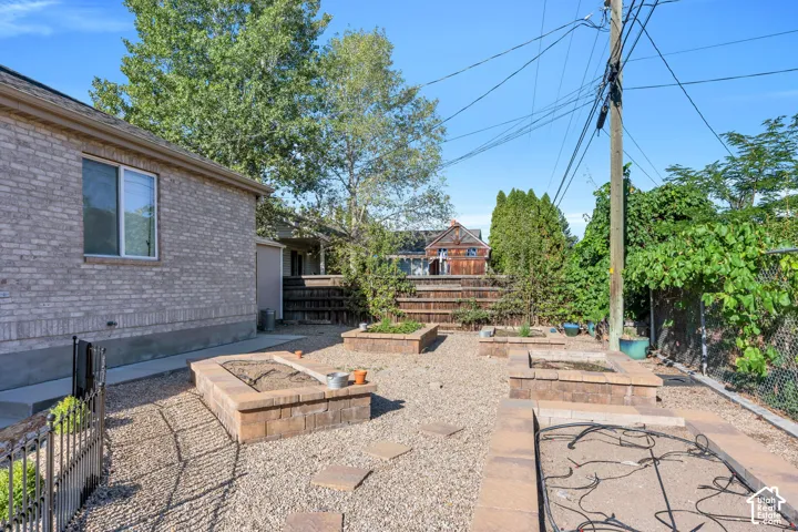Brick exterior with a single window, gravel ground cover, multiple stone-clad raised garden beds, and mature perimeter trees