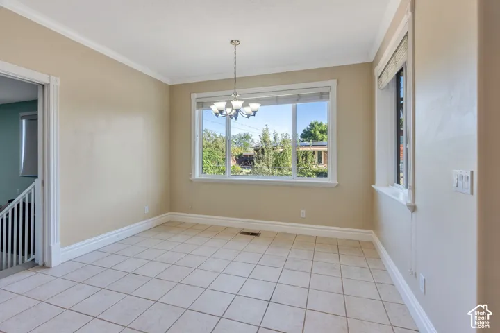Neutral tone wall paint, crown molding, tile flooring, a multi-pane window, and a chandelier