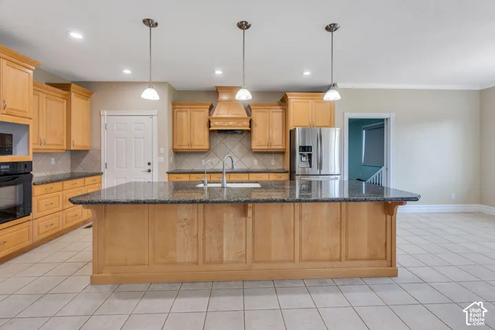 Kitchen featuring an expansive island with a dark countertop, stainless steel refrigerator, built-in oven, wood cabinetry, and tile flooring