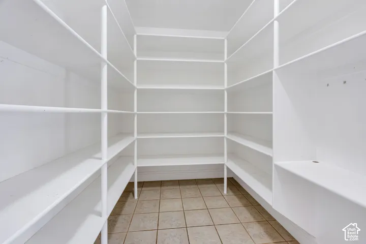 Spacious walk-in pantry featuring extensive white shelving, tiled flooring, and a built-in lower cabinet