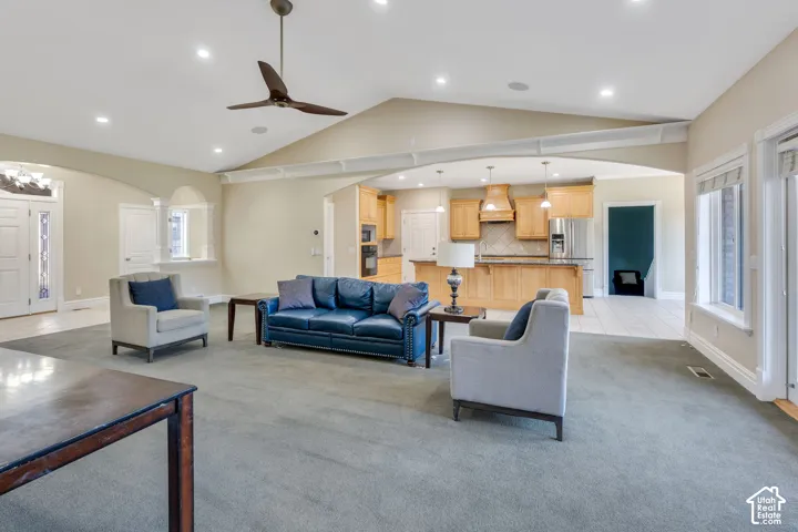 Vaulted ceiling with recessed lighting, ceiling fan, arched doorways, kitchen with light wood cabinetry, and double entry doors