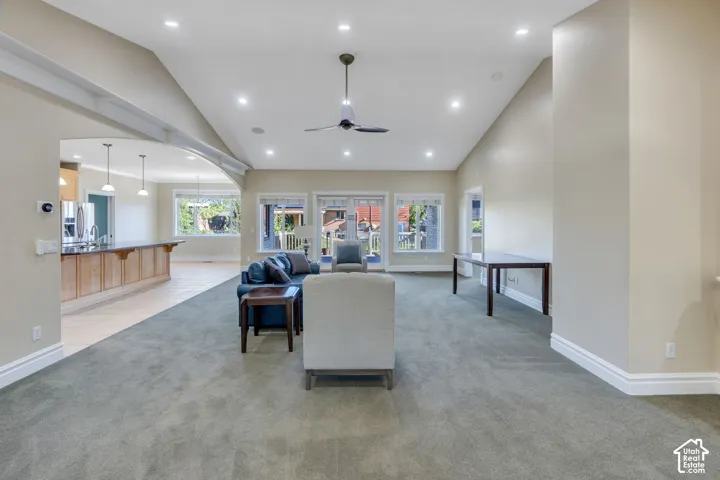 Vaulted ceiling with recessed lighting and a ceiling fan, multiple windows, and an arched doorway leading to the kitchen featuring pendant lighting