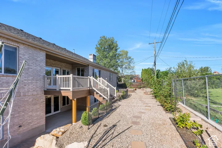 Brick exterior featuring a wood-finish deck with white railings, a concrete patio, and a gravel pathway with stepping stones