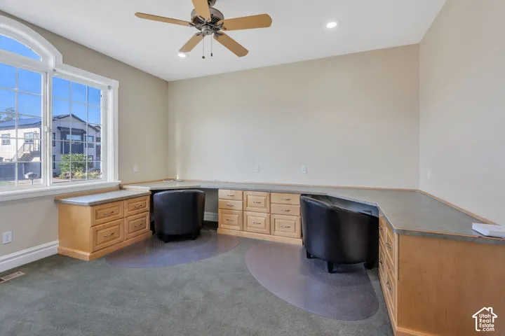 Arched window, built-in desk with storage, recessed lighting, ceiling fan, and carpeted flooring