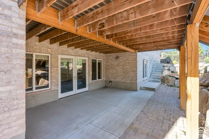 Covered patio area with concrete and paver flooring, supported by exposed wood beams and columns