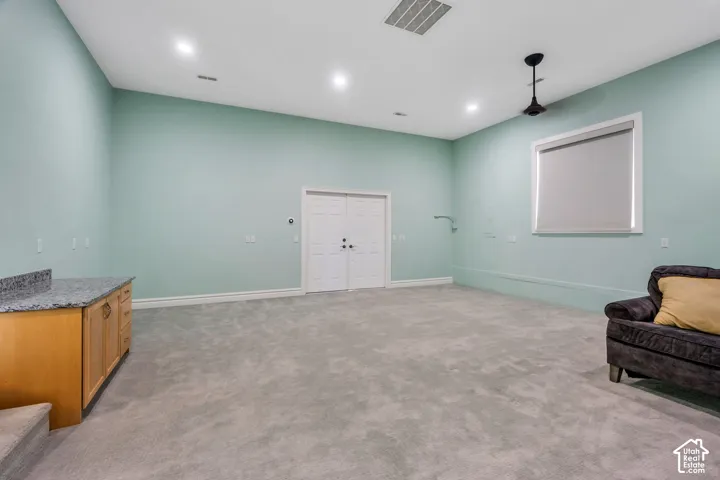 Spacious room with recessed lighting, light-colored walls, gray carpeting, and a built-in wood-finish cabinet with a granite-look countertop