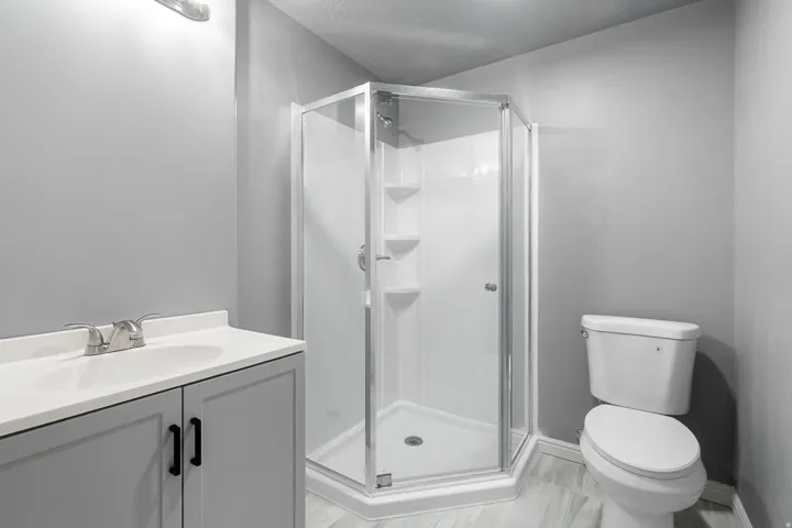 White vanity with a single basin sink, chrome faucet, and gray cabinetry with black hardware