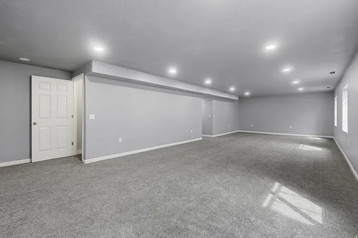 Expansive room featuring recessed lighting, gray carpeting, a six-panel interior door, and window openings