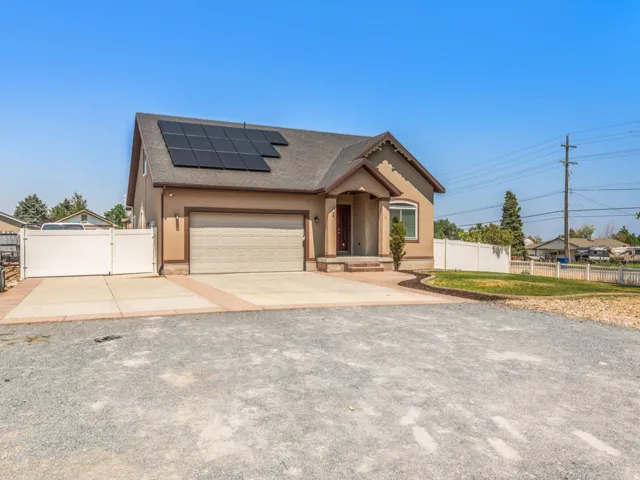 Modern single-story home featuring a spacious driveway with circular turnaround, neutral tan exterior with brick accents, dual-bay garage with paneled doors, and solar panel array on the roof