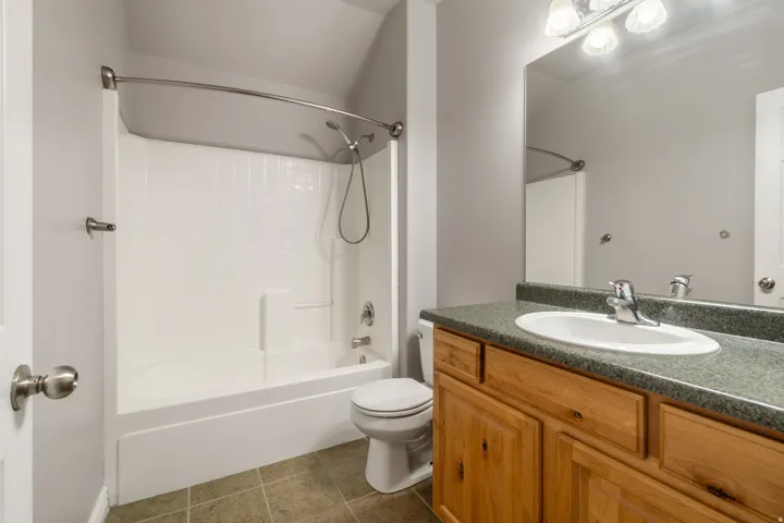 Full bathroom featuring a white tub/shower combination, a wood-finish vanity with a single basin sink, a large wall-mounted mirror, and tile flooring