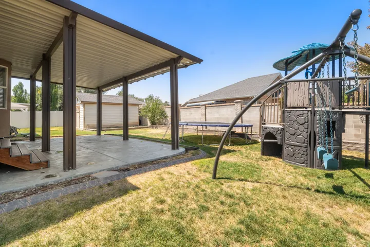Expansive covered patio with metal beam construction and concrete flooring, overlooking a manicured lawn with mature landscaping