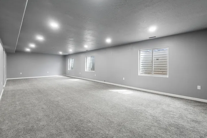 Spacious room with gray carpeting, recessed ceiling lighting, and multiple windows