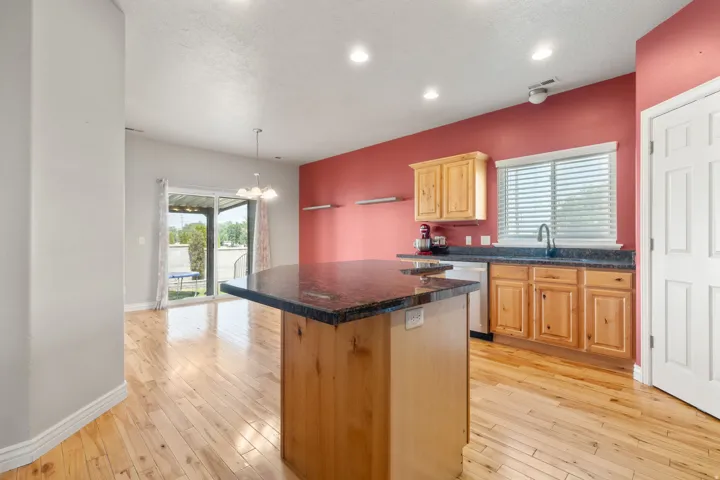 Kitchen featuring a central island with a stone countertop, light wood cabinetry, wood-finish flooring, and stainless steel appliances
