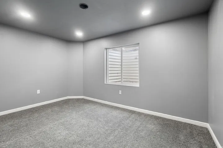 Recessed lighting, gray carpeting, gray walls, white trim, and a window with a window well