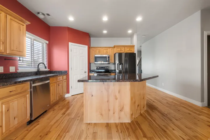 Kitchen featuring wood-finish cabinetry, stainless steel appliances, granite-style countertops, wood-finish flooring, and recessed lighting