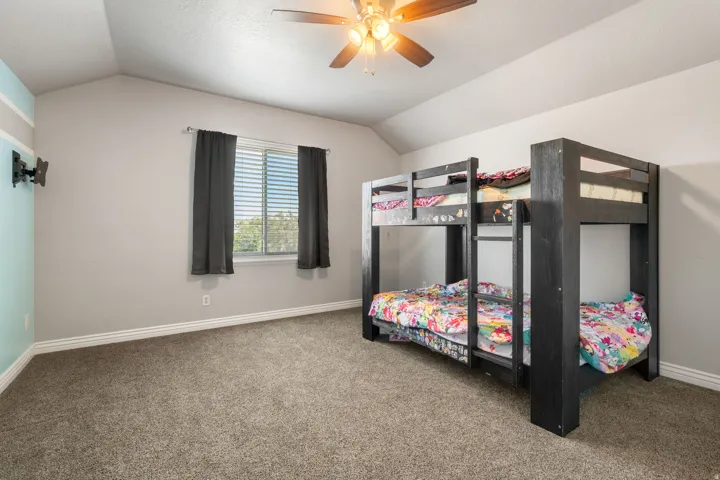 Vaulted ceiling with a ceiling fan, carpeted flooring, and a window with blinds