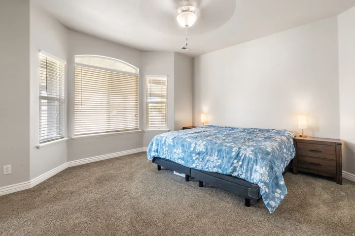 Bay window with arched transom, textured carpet flooring, ceiling fan with light fixture, and white trim