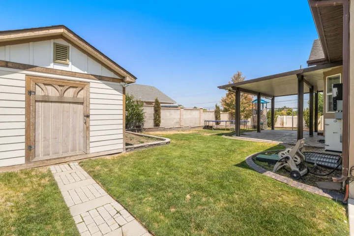 Expansive backyard featuring a manicured lawn, a detached storage shed with a wooden door, a covered patio area, and concrete block retaining walls