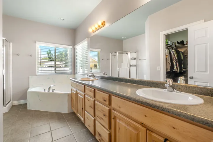 Spa-inspired primary bathroom showcasing a wood-finish vanity with dual sinks, quartz countertop, and brushed nickel fixtures