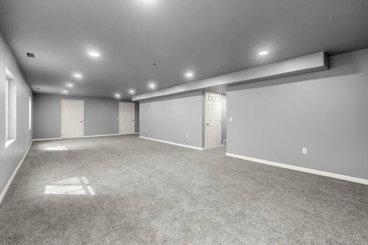 Expansive room featuring gray carpeting, recessed ceiling lighting, and multiple paneled doors