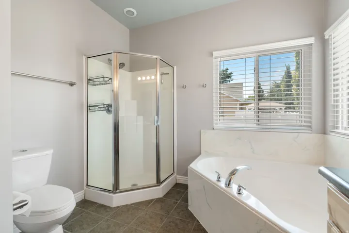 White soaking tub, glass-enclosed shower, tile flooring, window with blinds, and recessed lighting