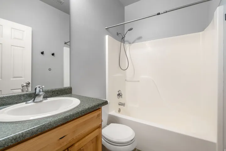 Bathroom featuring a vanity with an integrated sink, a gray speckled countertop, light wood-finish cabinetry, and a white fiberglass shower/tub combination