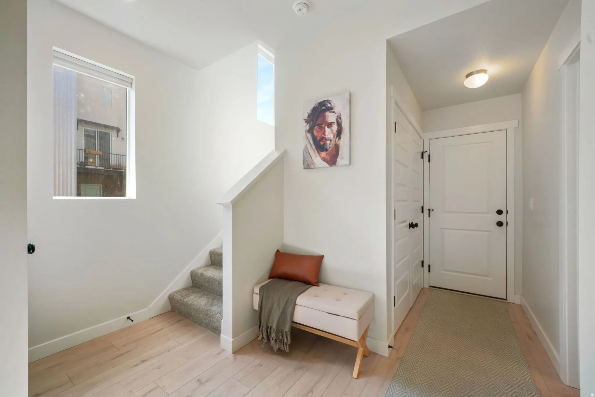 Light wood-finish flooring, white paneled doors with matte black hardware, and an interior staircase with carpeted treads