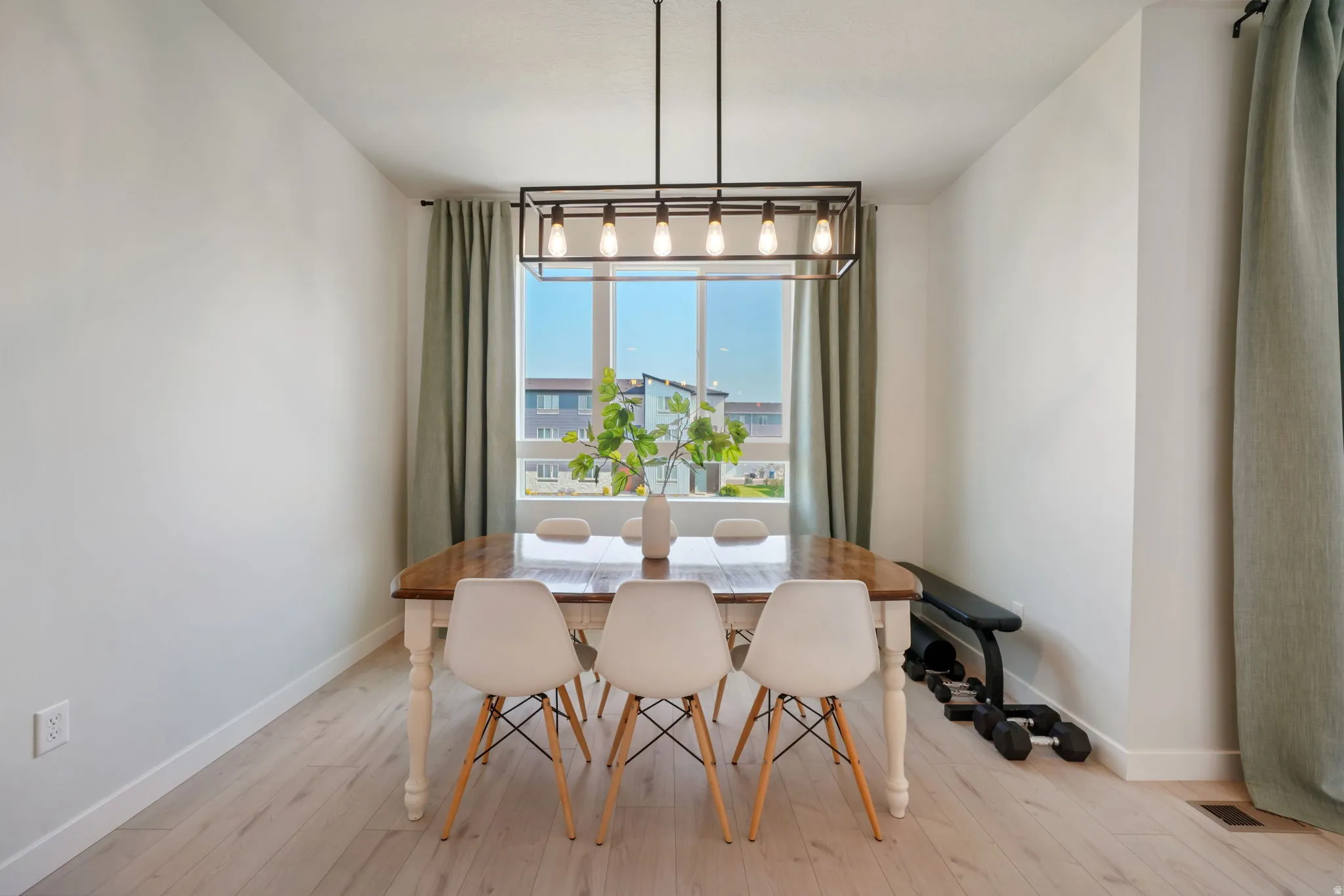 Light wood-finish flooring, rectangular window with trim, contemporary linear chandelier, and light-toned wall finishes