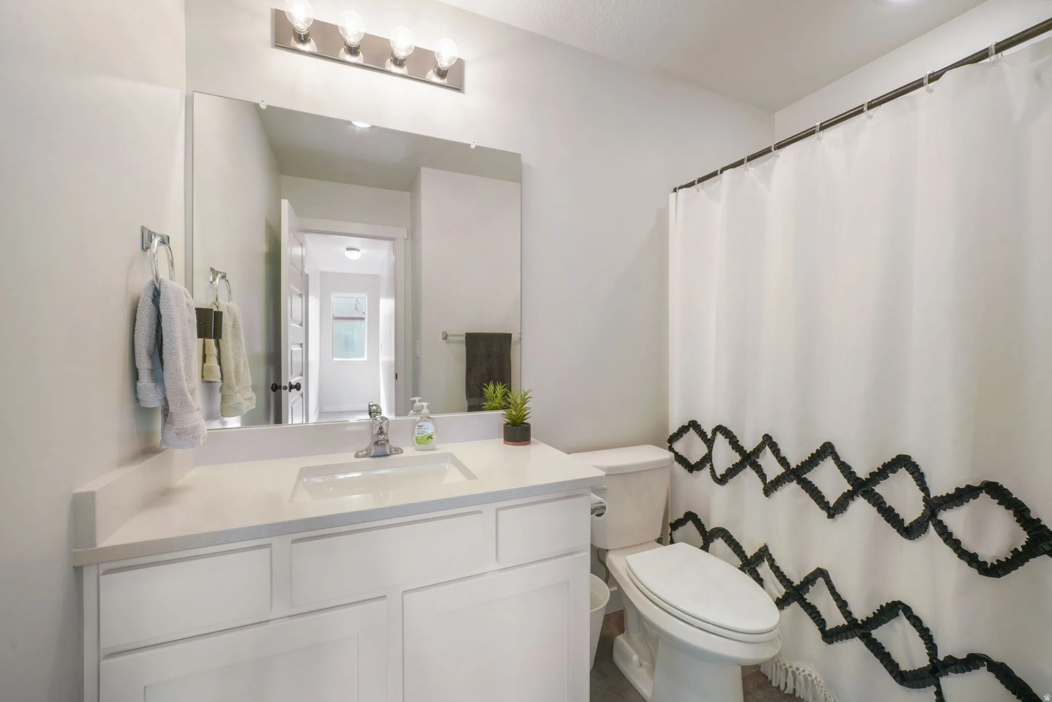 Bathroom featuring a white vanity with an integrated sink, a rectangular mirror, a four-bulb vanity light, and a toilet