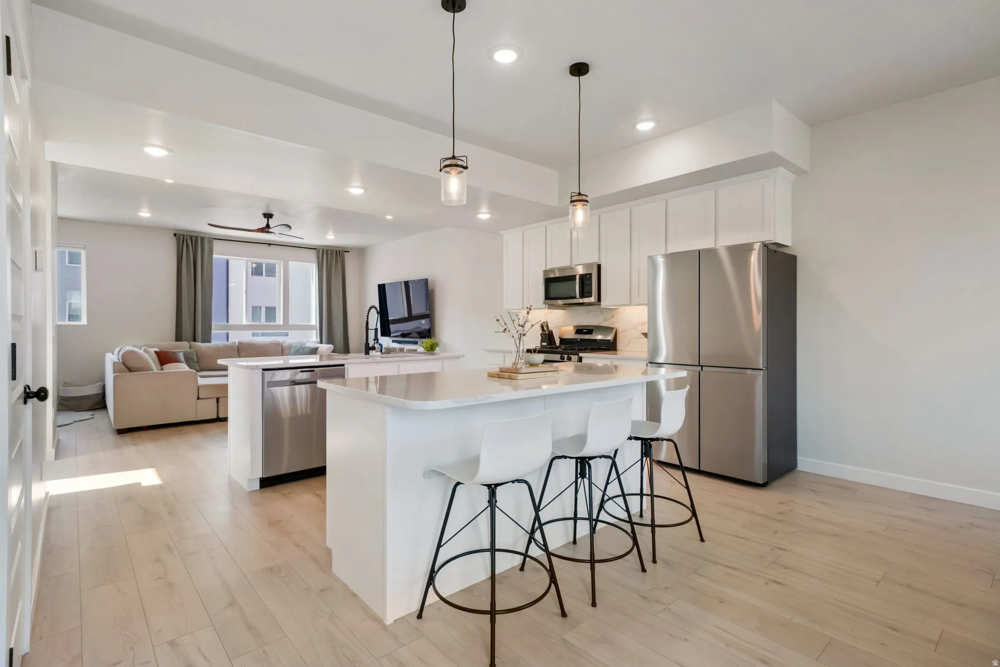 Open-concept living space featuring wood-finish flooring, recessed lighting, white cabinetry, stainless steel appliances, and a kitchen island with pendant lighting