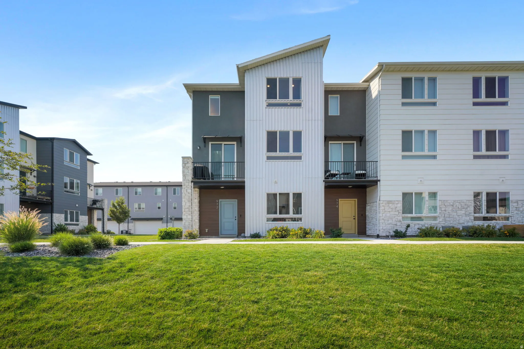 Contemporary multi-level exterior with varied siding textures, stone veneer accents, individual balconies, and a manicured lawn