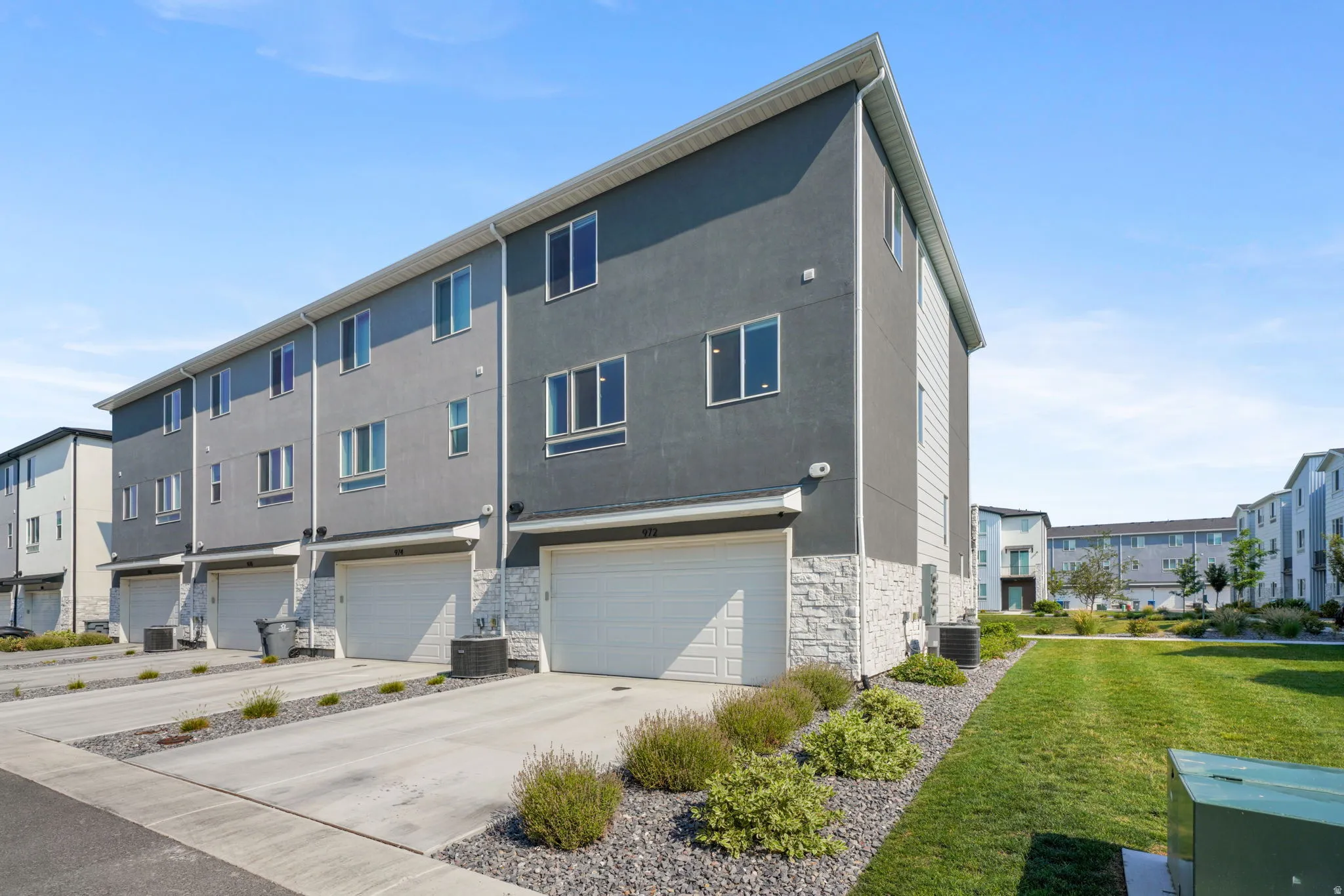 Modern townhome exterior with a dark gray facade, stone veneer detailing, multiple windows, and an attached garage