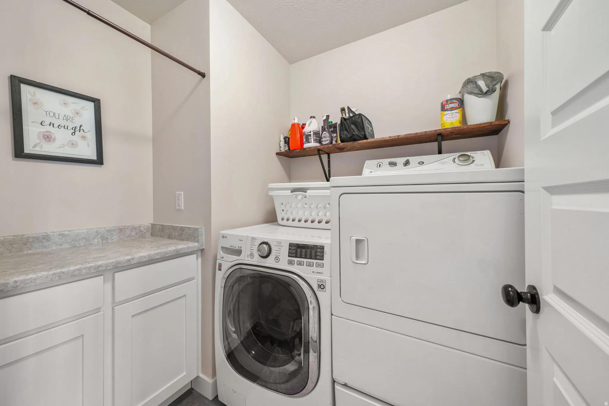 Dedicated laundry room featuring a built-in folding counter, white cabinetry, a wood-finish floating shelf, and a hanging rod