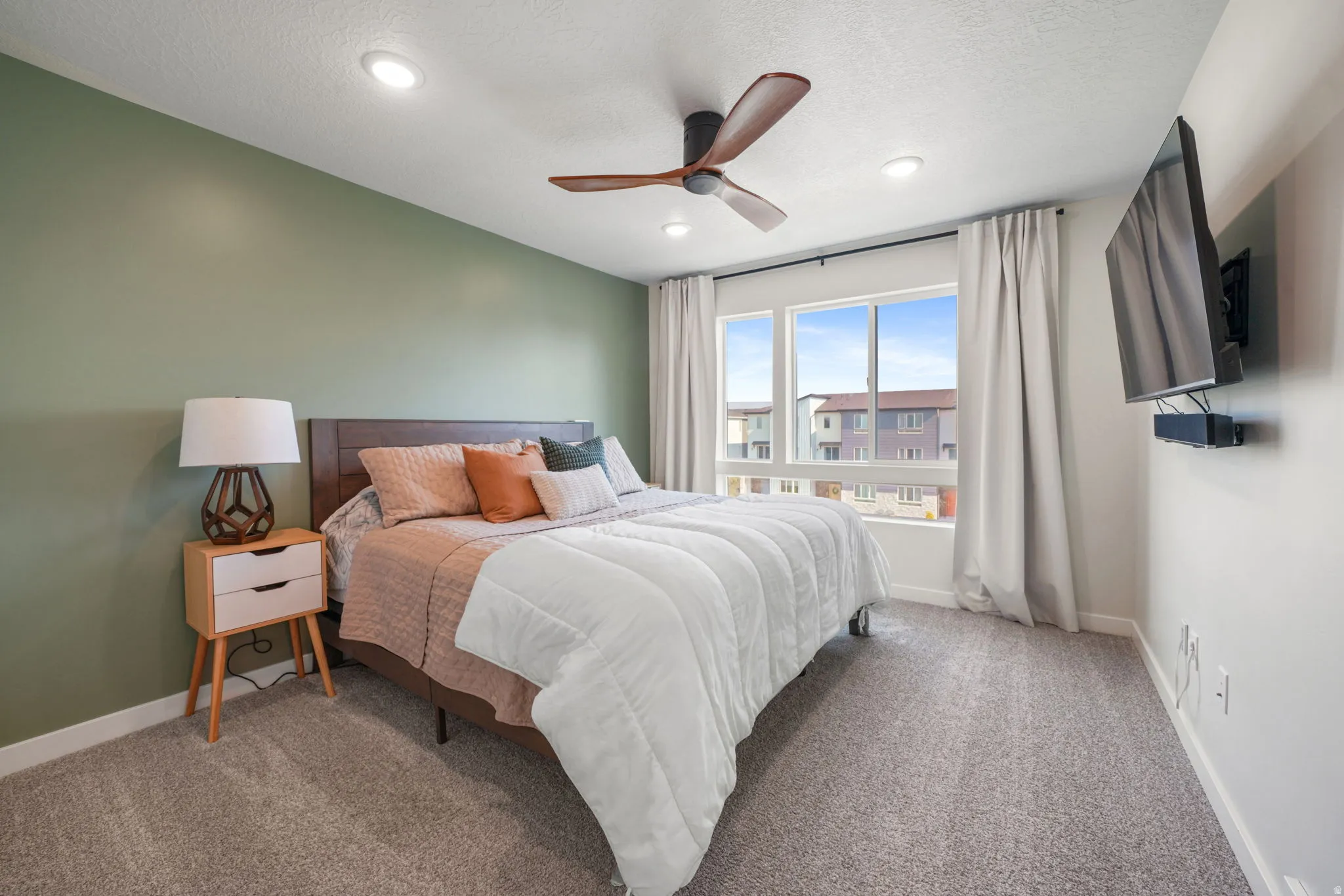 Recessed lighting, ceiling fan, large windows, wall-mounted television, and carpet flooring