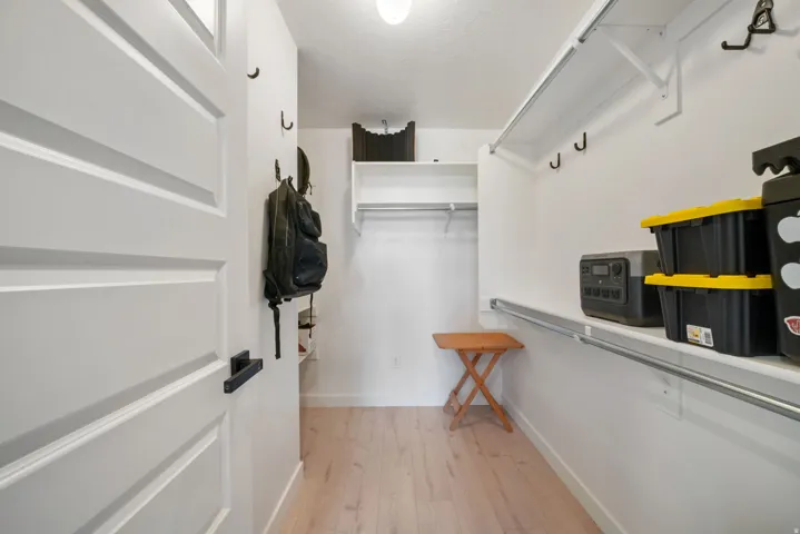 Walk-in closet featuring light wood-finish flooring, white walls, and built-in shelving with hanging rods