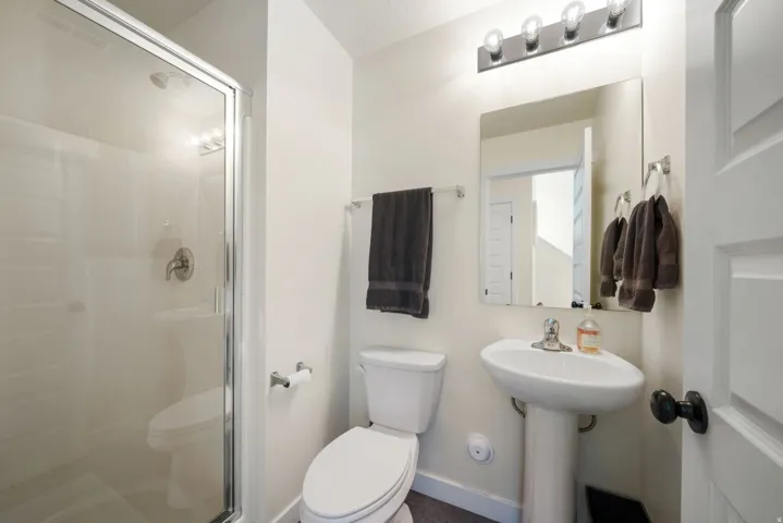 Pedestal sink, wall-mounted mirror, four-bulb vanity light, and a toilet with a shower enclosure