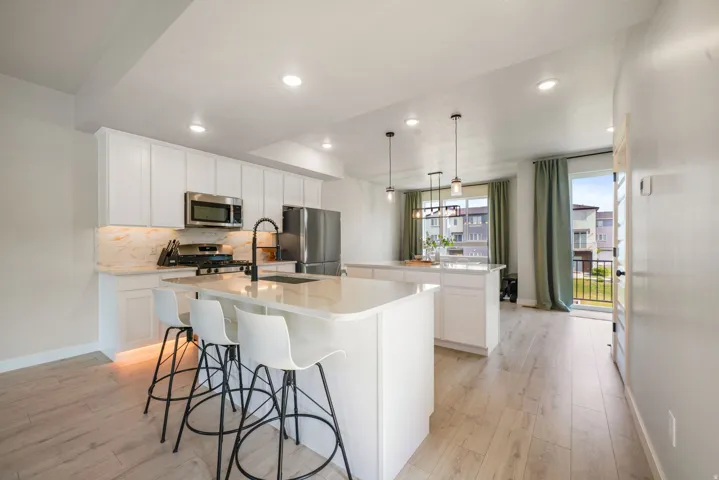 White cabinetry with brushed nickel hardware, stainless steel appliances, light-toned wood-finish flooring, recessed lighting, and a kitchen island with seating