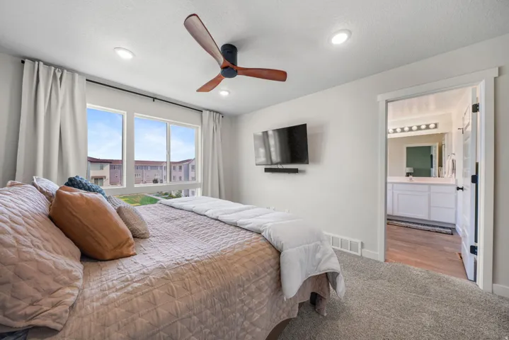 Recessed lighting, ceiling fan with wood-finish blades, large windows, and an open doorway to a bathroom with a white vanity and wood-finish flooring
