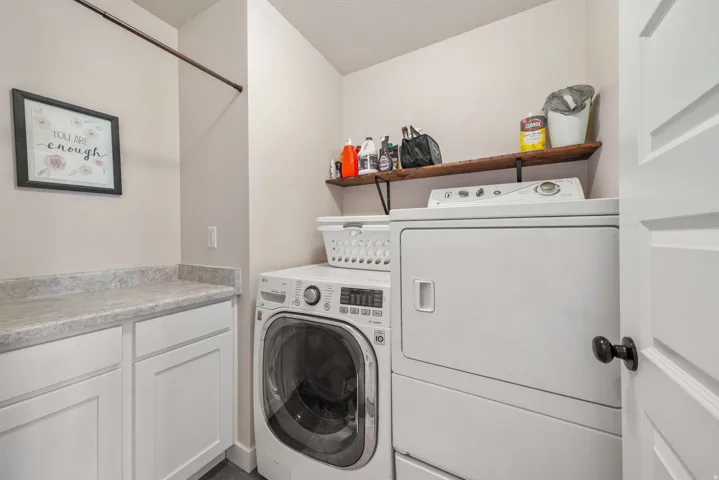 Dedicated laundry room featuring a built-in folding counter, white cabinetry, a wood-finish floating shelf, and a hanging rod