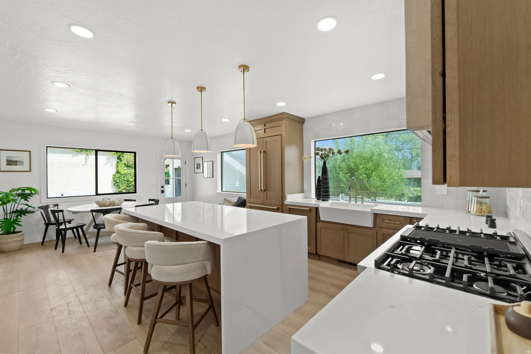 Bright kitchen featuring recessed lighting, light wood-finish flooring, a center island with pendant lighting, a farmhouse sink, and a gas range