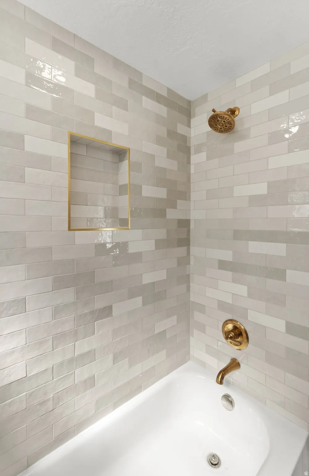 White porcelain bathtub with a built-in niche, gold-finish fixtures, and subway-style tile surround