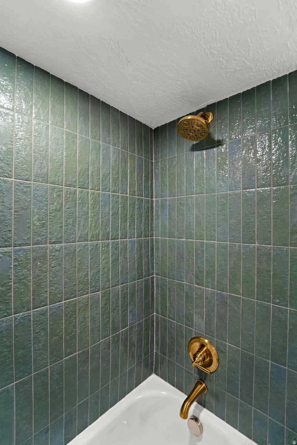 Porcelain bathtub with teal tile surround and brass fixtures