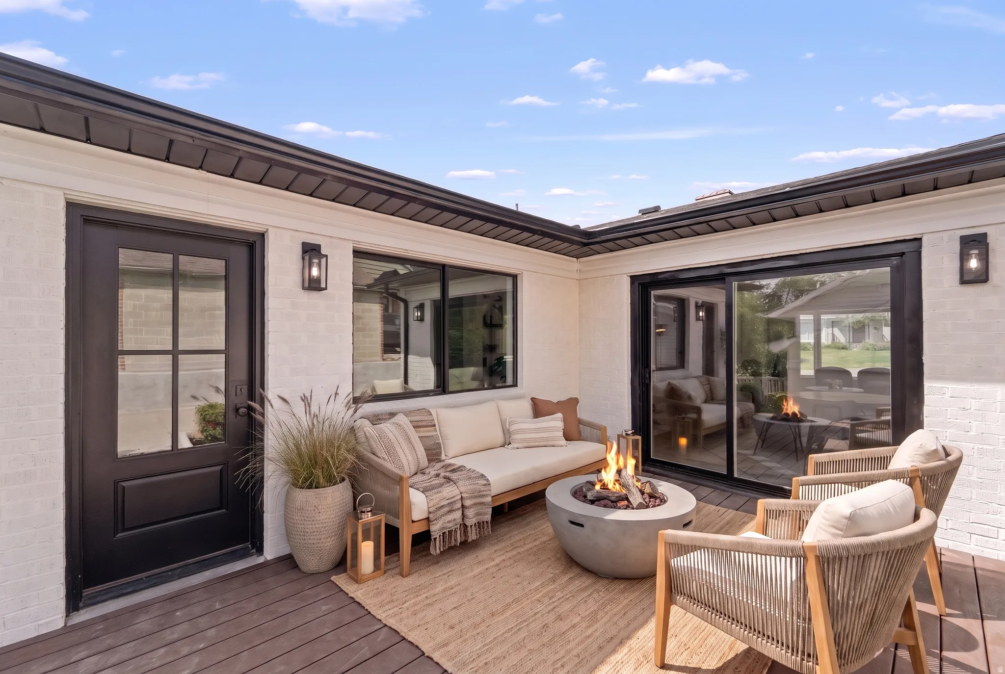 Outdoor deck space featuring a built-in fire pit, white brick exterior, black-framed windows, and a black-framed glass-paned door
