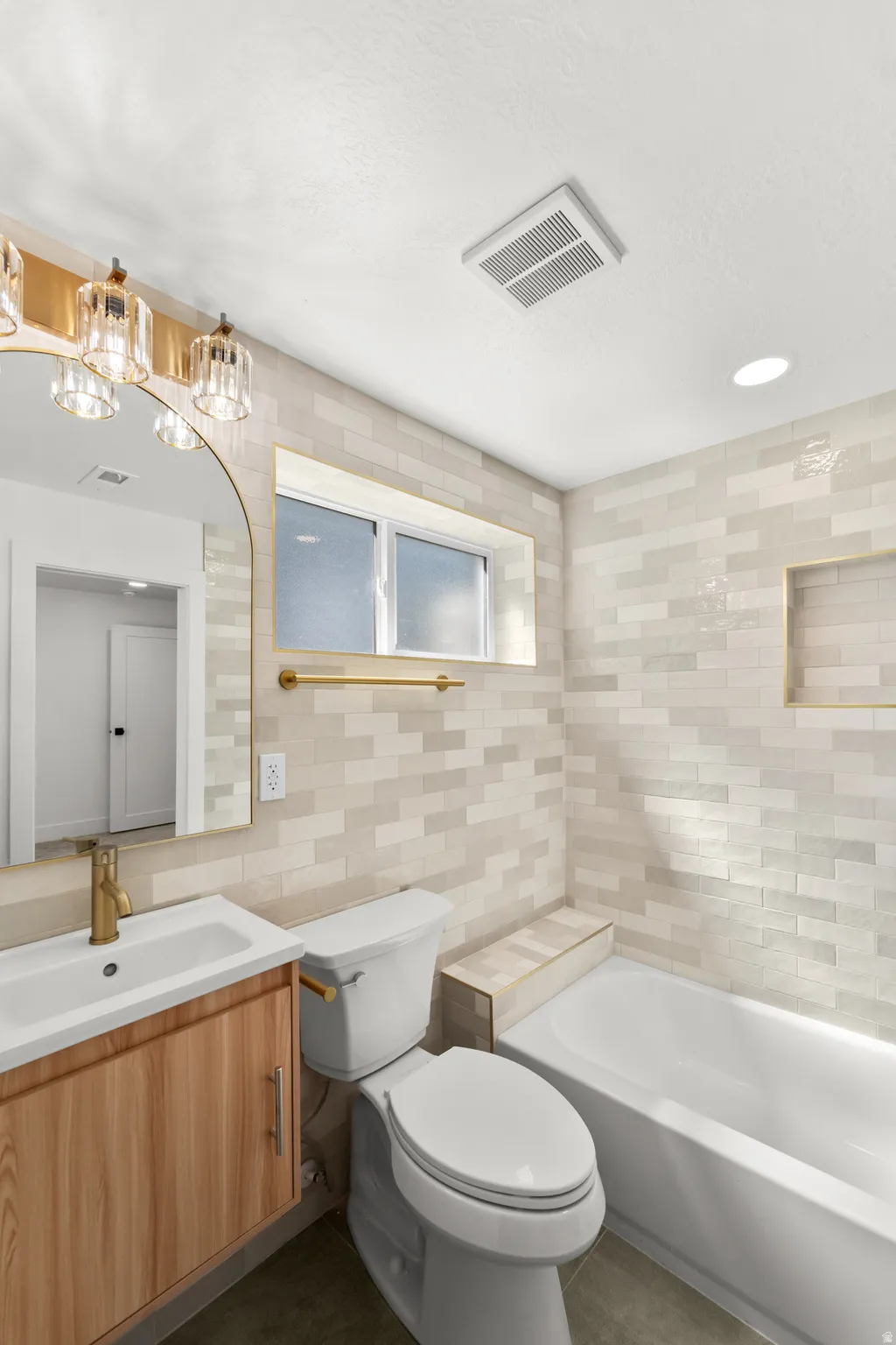 Bathroom featuring a wall-mounted vanity with a single basin, a toilet, a built-in bathtub, and a tiled accent wall