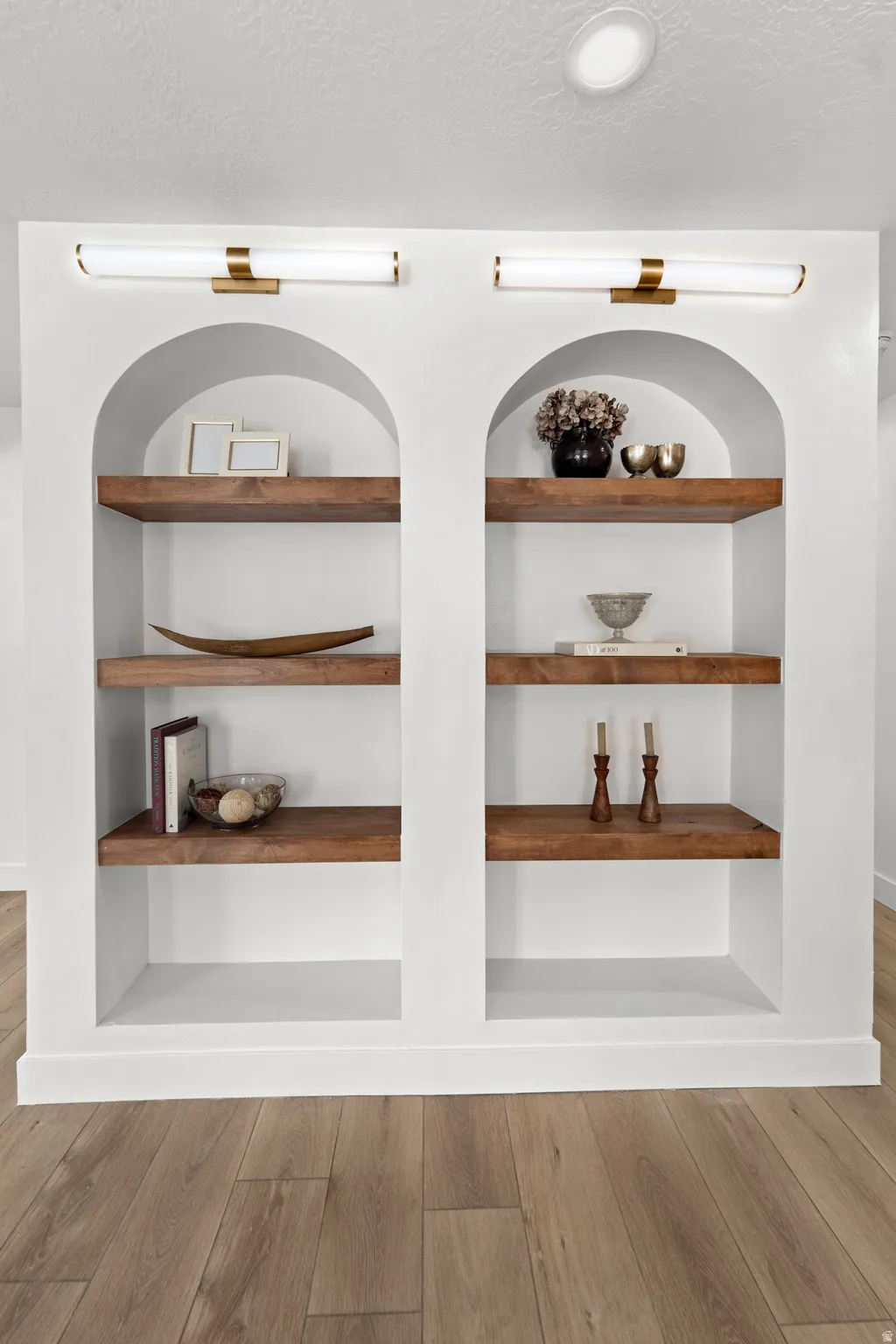 Built-in arched shelving with wood-finish shelves, integrated lighting, and wood-finish flooring