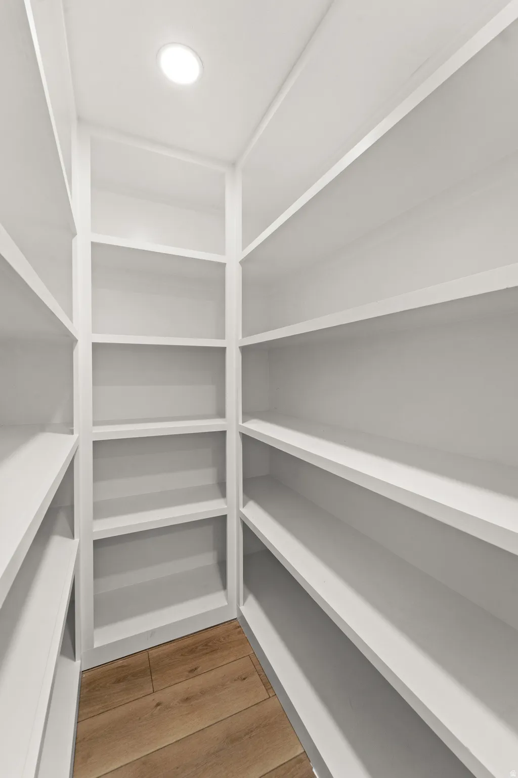 Walk-in pantry featuring extensive white shelving and wood-finish flooring with recessed lighting