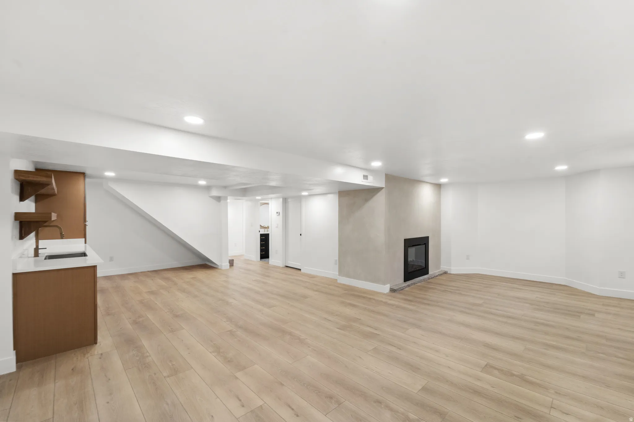 Open-concept living space featuring engineered wood-finish flooring throughout, recessed ceiling lighting, and a modern kitchen with wood cabinetry and stainless steel appliances